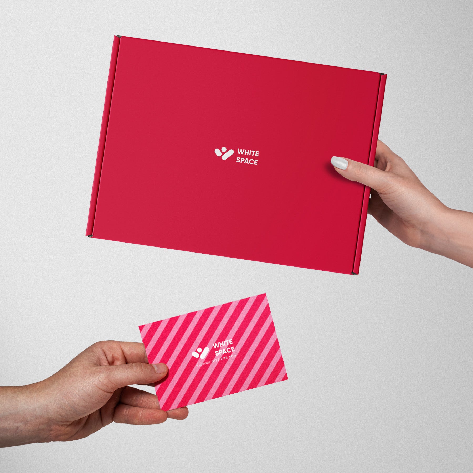 Hands exchanging a red gift box and a pink striped card, both branded with the White Space logo, showcasing an elegant and festive packaging design.